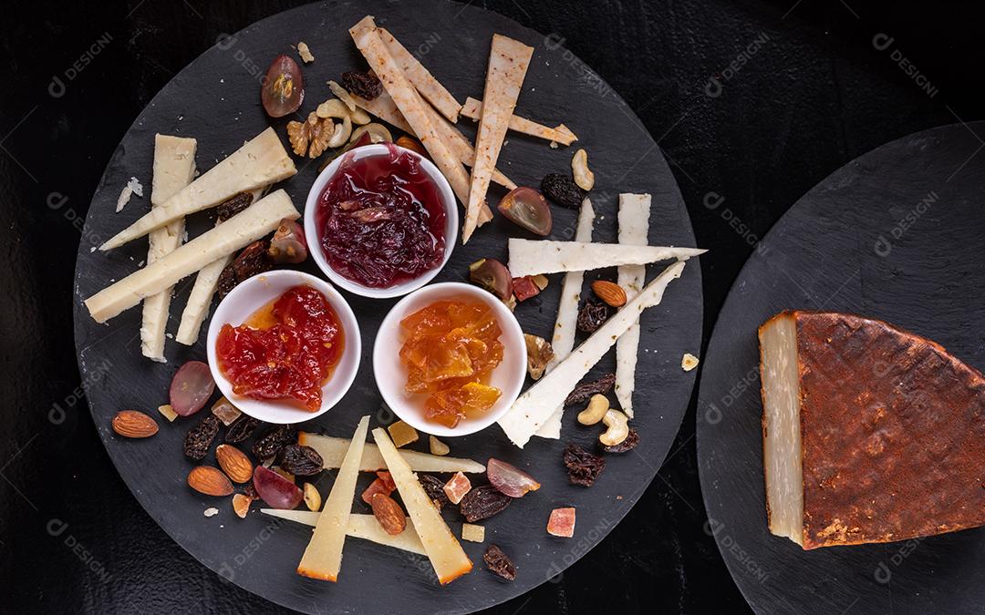 Tábua de queijos com nozes e marmeladas em um fundo de ardósia preta