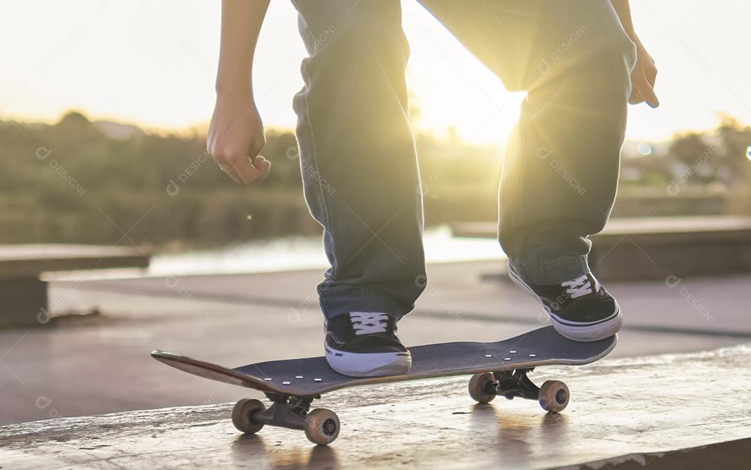 Skatista adolescente realizando um truque com um skate em um pôr do sol