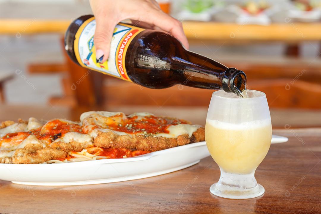 Mãos de pesosas colocando cerveja sobre o seu copo prato de comida mesa madeira