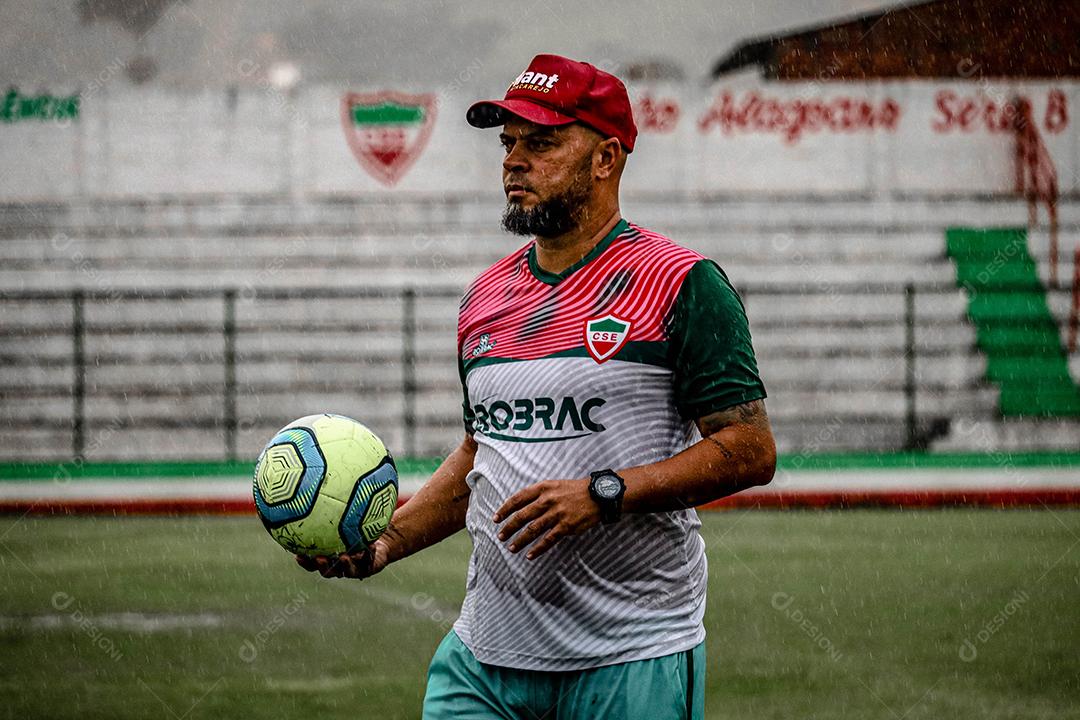 Treinador segurando bola de futebol sobre campo de esporte