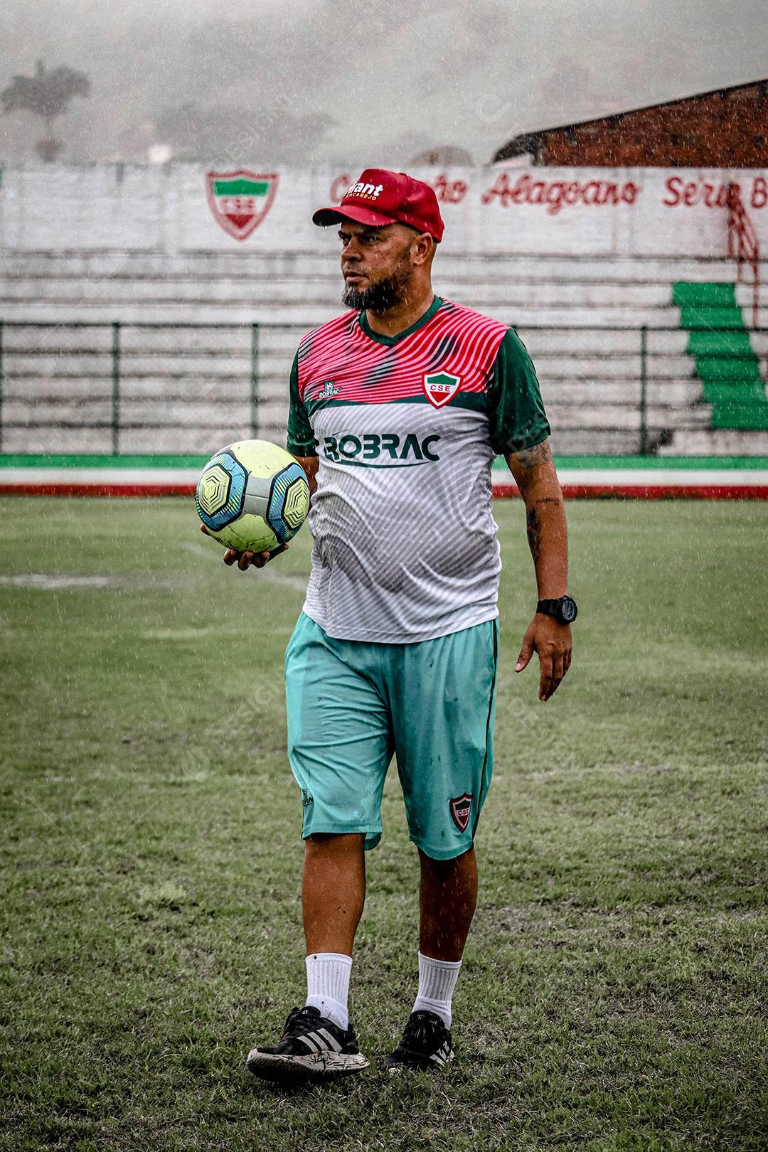 Treinador segurando bola de futebol sobre campo de esporte