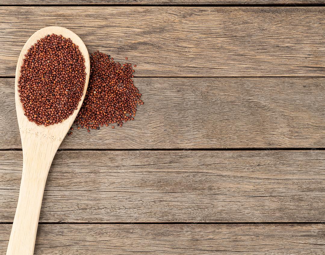 Quinoa vermelha crua em uma colher sobre a mesa de madeira