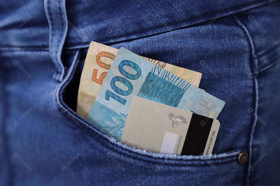 Dinheiro brasileiro real sobre um bolso cartão de credito de uma calça de uma pessoas brasileira
