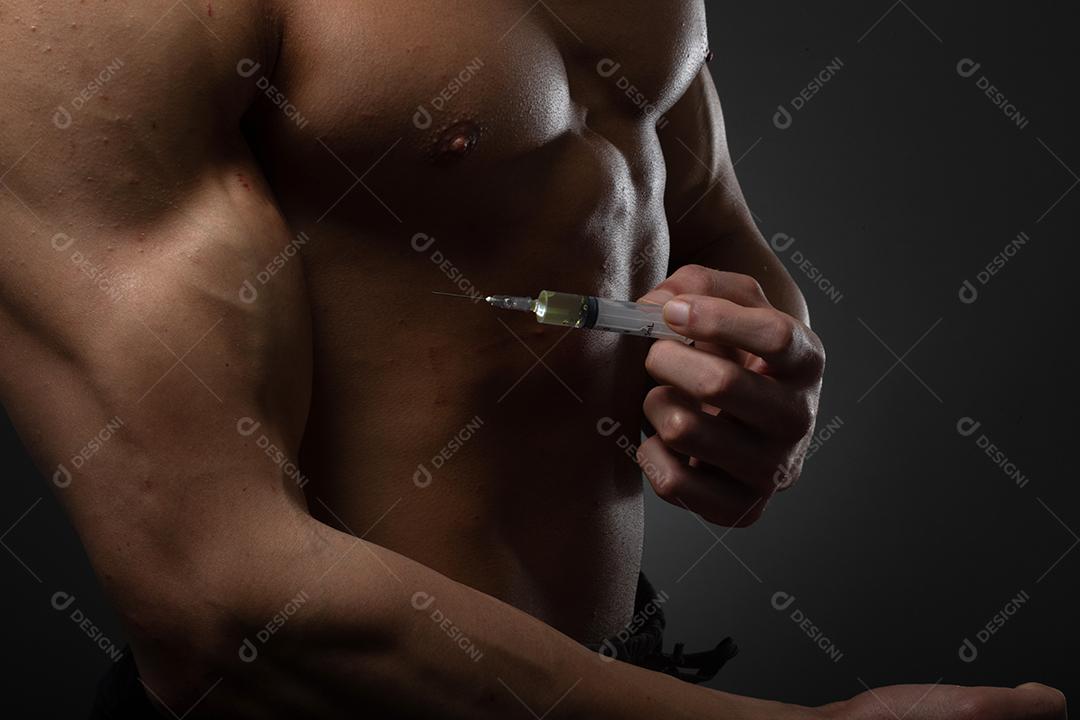 Homem musculoso com uma seringa na mão. Usuário de esteróides anabolizantes para treinamento de força.
