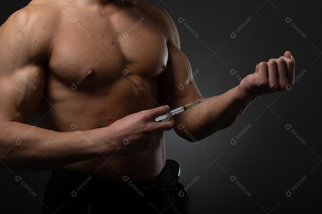Homem musculoso com uma seringa na mão. Usuário de esteróides anabolizantes para treinamento de força.
