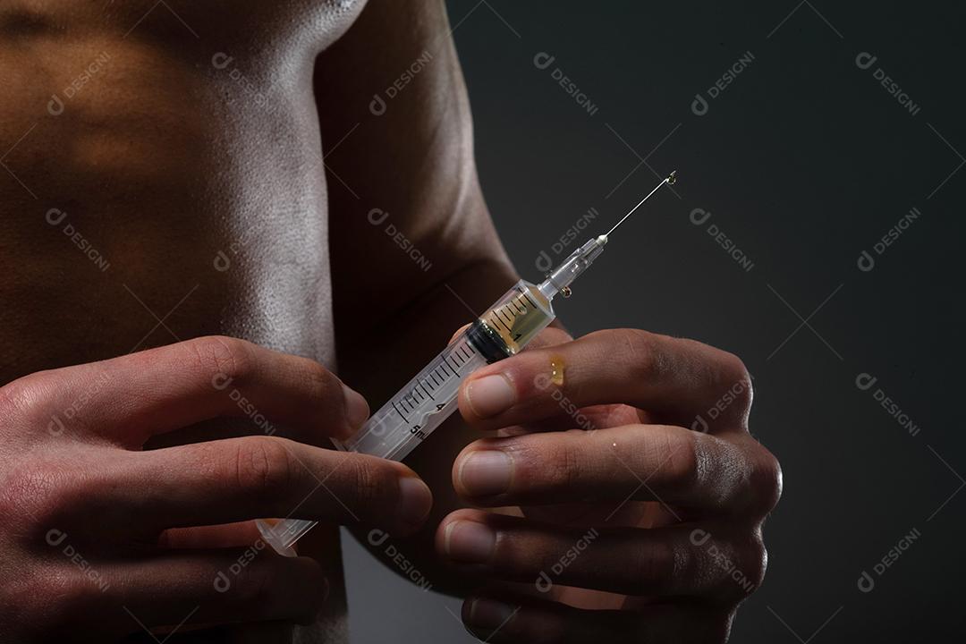 Homem musculoso com uma seringa na mão. Usuário de esteróides anabolizantes para treinamento de força.