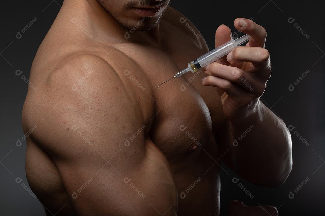 Homem musculoso com uma seringa na mão. Usuário de esteróides anabolizantes para treinamento de força.