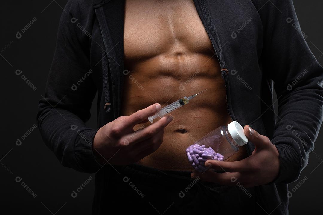 Homem musculoso com uma seringa na mão. Usuário de esteróides anabolizantes para treinamento de força.