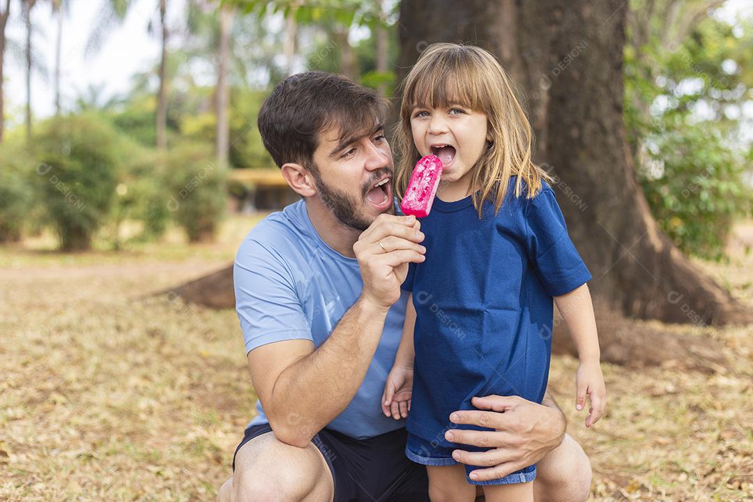 Pai e filha no parque chupando um delicioso picolé