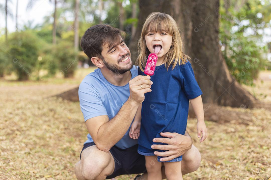 Pai e filha no parque chupando um delicioso picolé