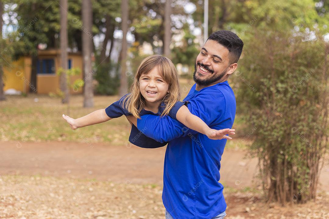 Pai e filha sorrindo para a câmera no parque. Filha sobe nas costas do papai. Feliz dia dos pais