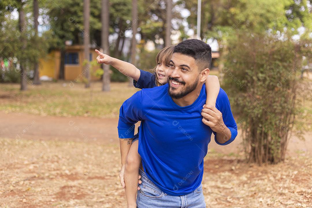 Pai e filha sorrindo para a câmera no parque. Filha sobe nas costas do papai. Feliz dia dos pais
