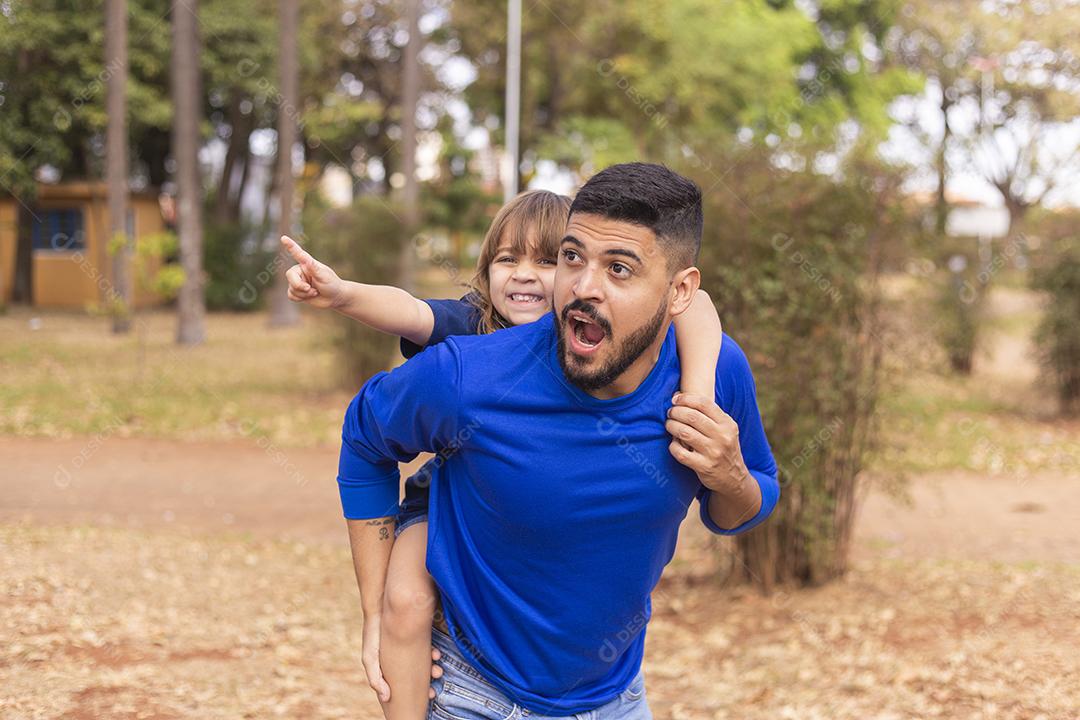 Pai e filha sorrindo para a câmera no parque. Filha sobe nas costas do papai. Feliz dia dos pais