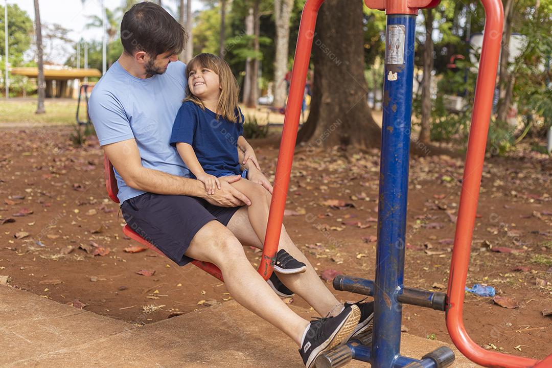 pai e filho fazendo exercício em aparelhos ao ar livre com a filha.