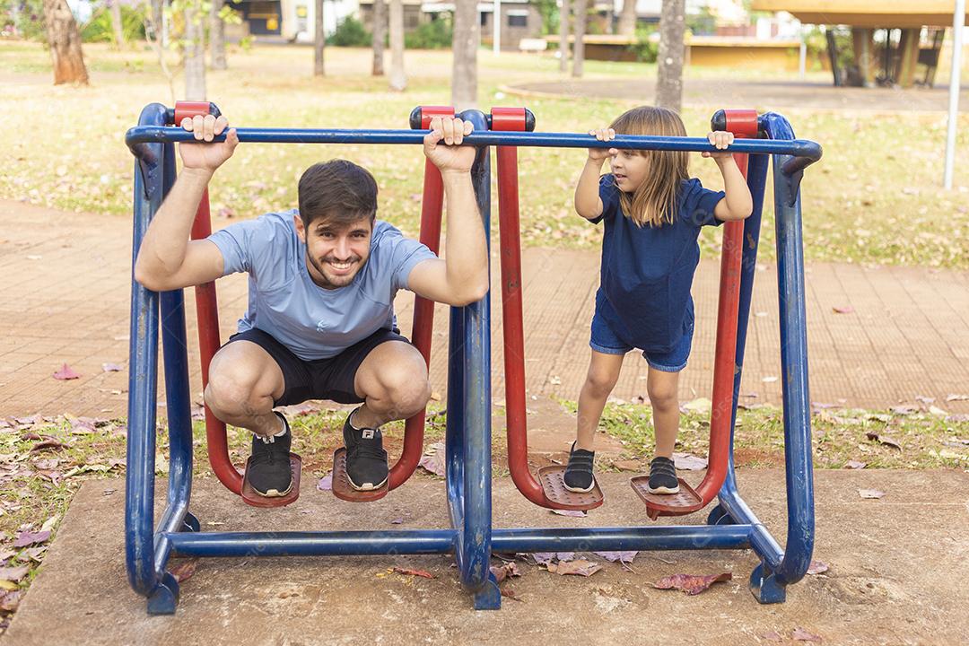 pai e filho fazendo exercício em aparelhos ao ar livre com a filha.
