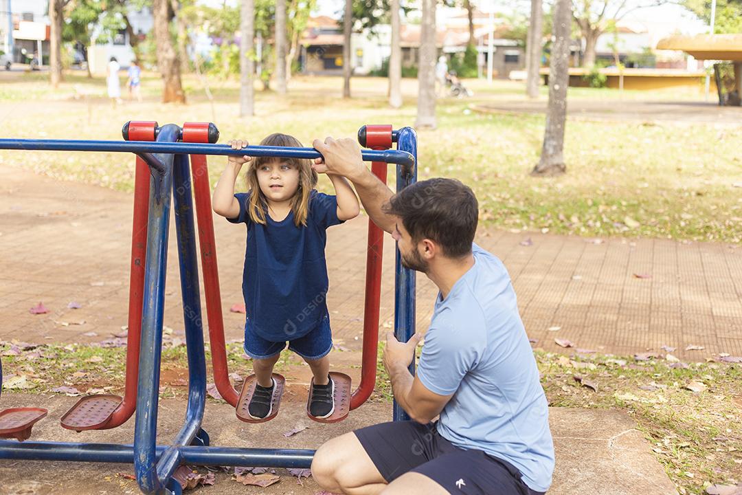 pai e filho fazendo exercício em aparelhos ao ar livre com a filha.