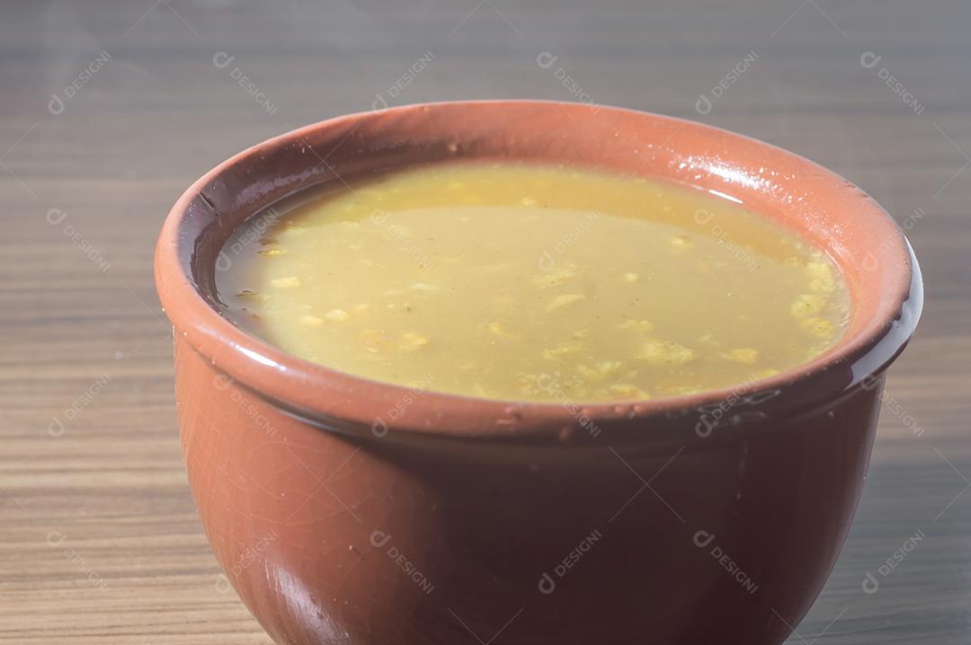 Sopa amarela em uma tigela de barro, a sopa está em uma mesa de madeira com espaço de cópia e colher.