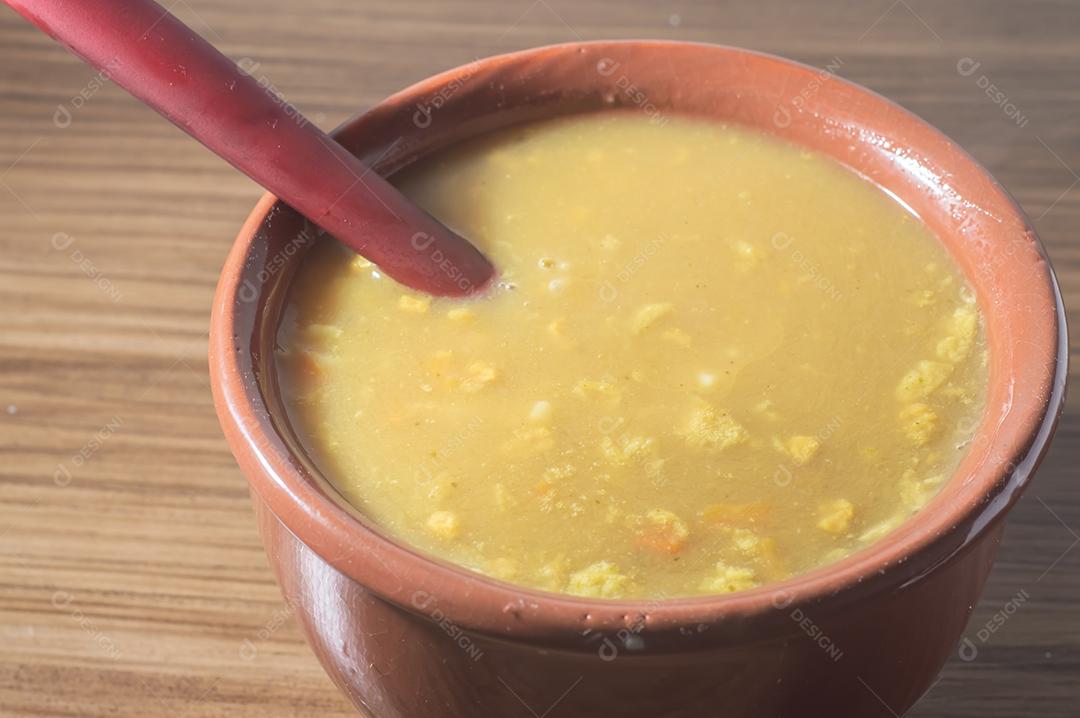 Sopa amarela em uma tigela de barro, a sopa está em uma mesa de madeira com espaço de cópia e colher.