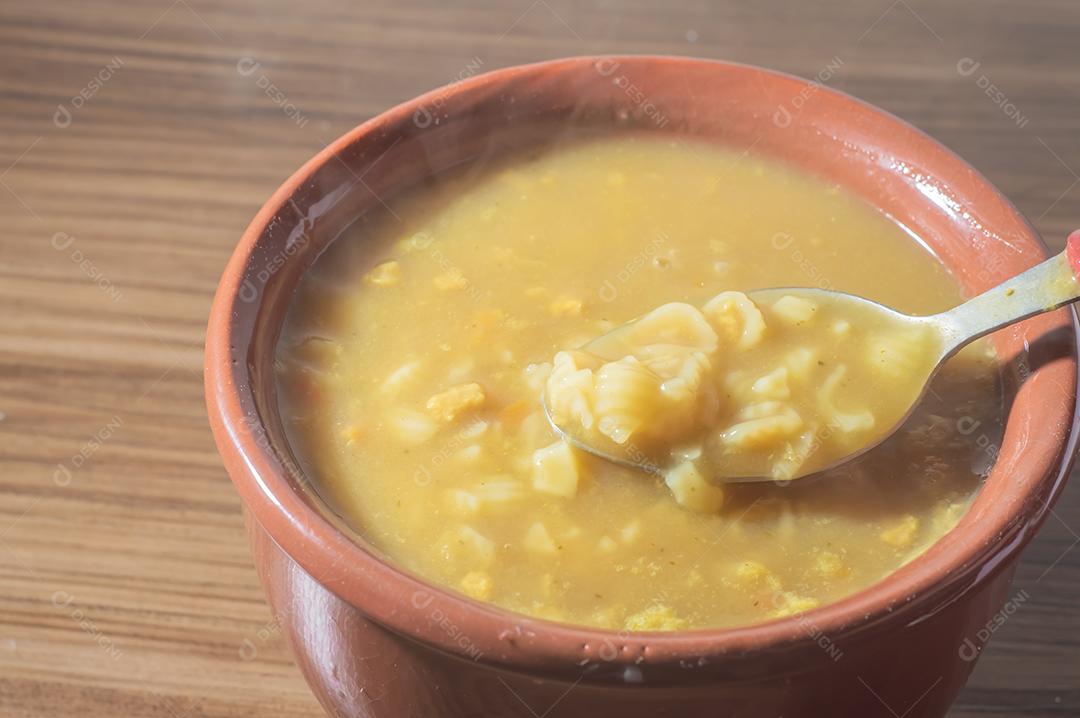 Sopa amarela em uma tigela de barro, a sopa está em uma mesa de madeira com espaço de cópia e colher.
