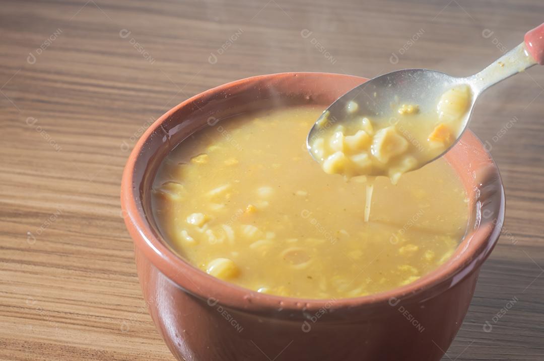 Sopa amarela em uma tigela de barro, a sopa está em uma mesa de madeira com espaço de cópia e colher.