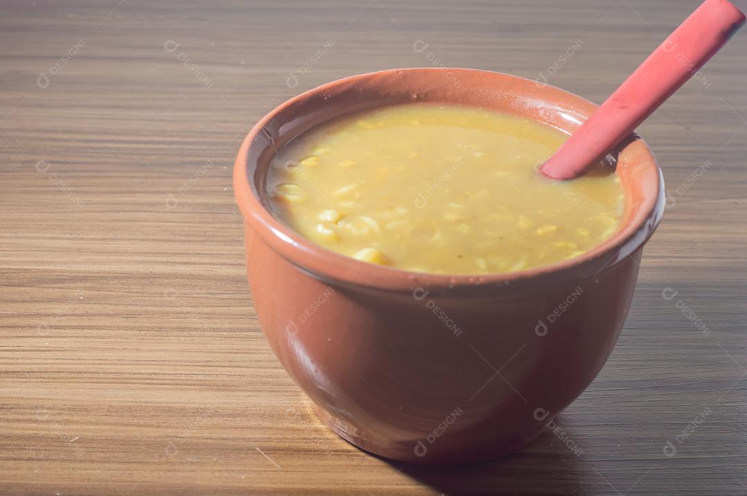 Sopa amarela em uma tigela de barro, a sopa está em uma mesa de madeira com espaço de cópia e colher.