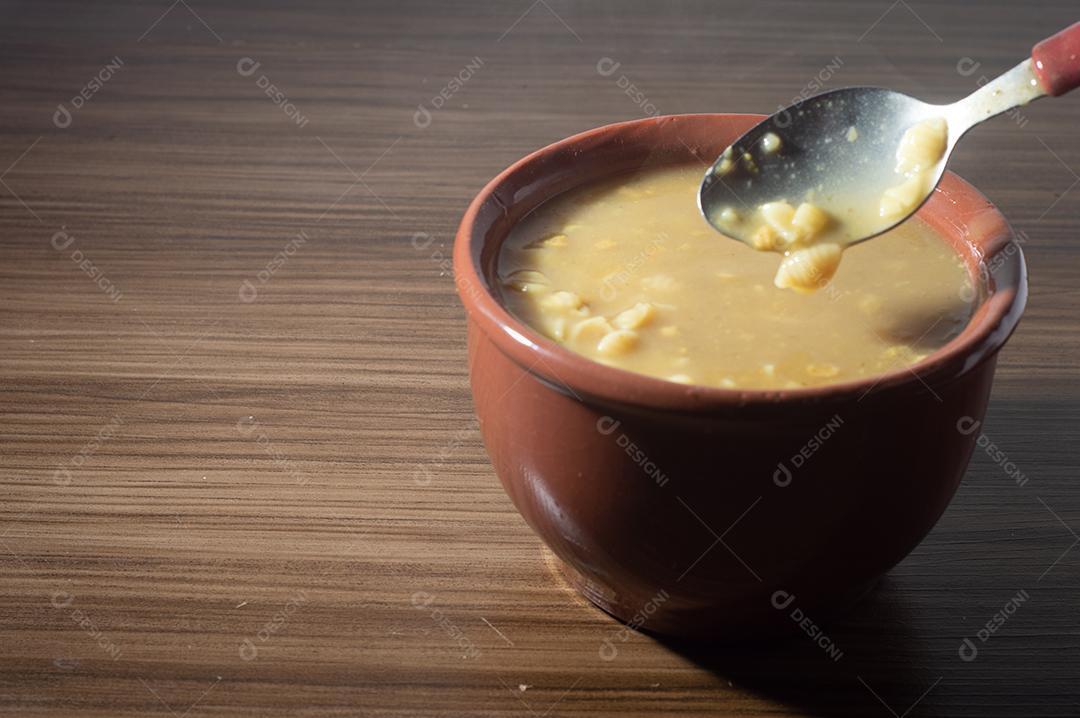 Sopa amarela em uma tigela de barro, a sopa está em uma mesa de madeira com espaço de cópia e colher.