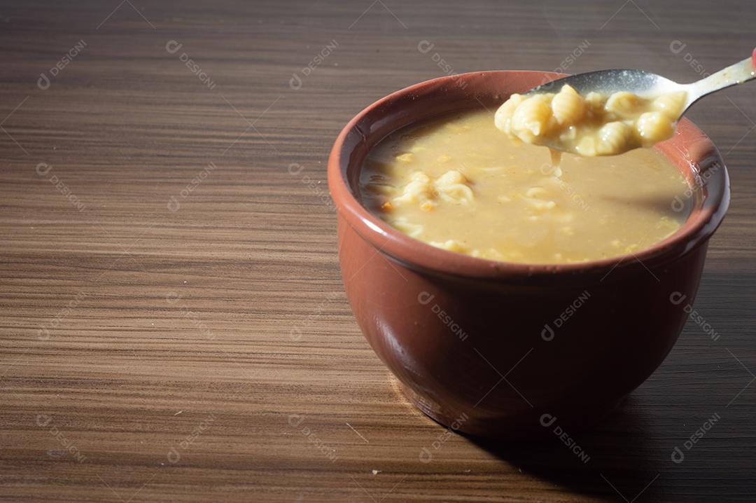 Sopa amarela em uma tigela de barro, a sopa está em uma mesa de madeira com espaço de cópia e colher.