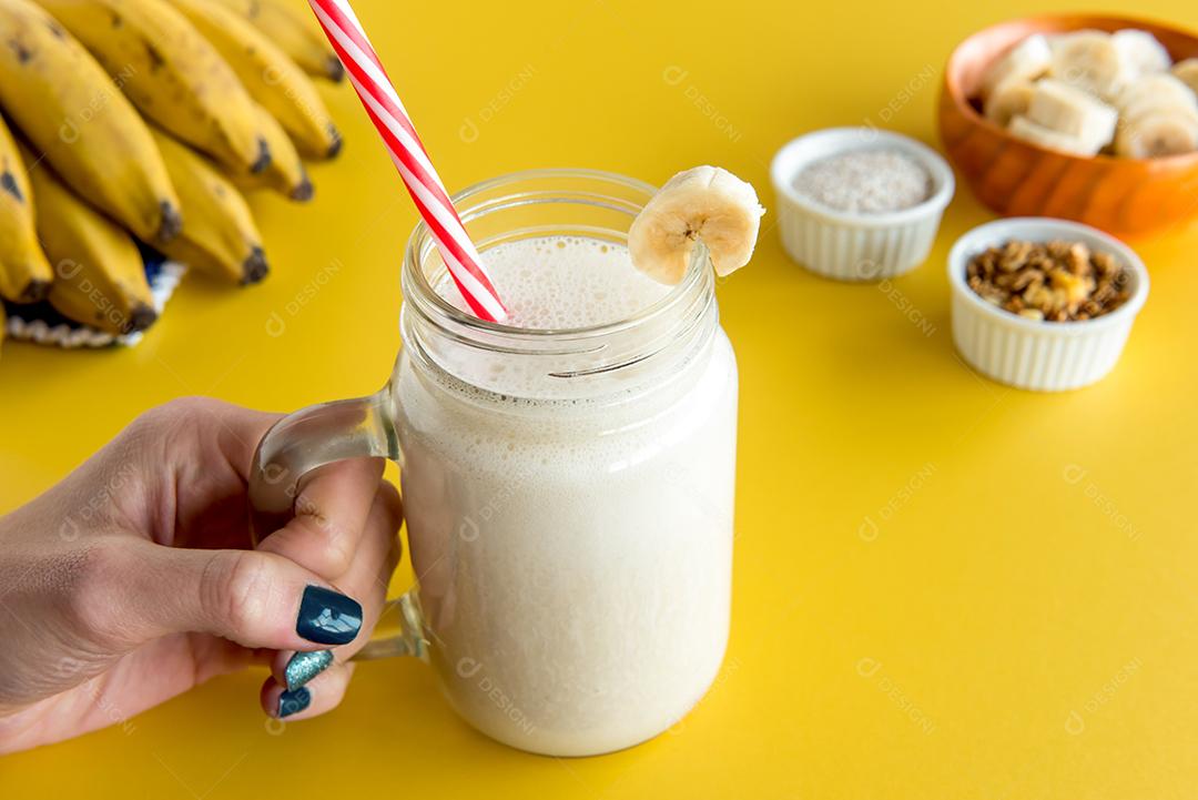 mão segurando um copo de smoothie de banana, shake saudável de banana com