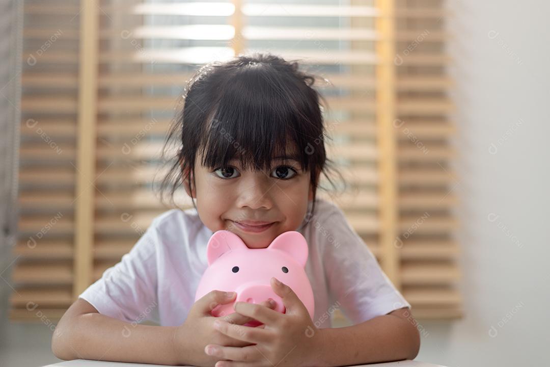 Menina asiática economizando dinheiro em um cofrinho, aprendendo sobre s