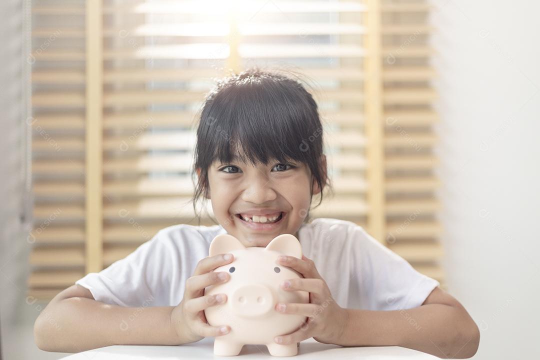 Menina asiática economizando dinheiro em um cofrinho, aprendendo sobre s