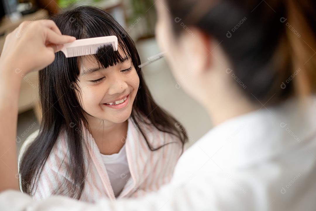 Mãe asiática cortando cabelo para sua filha na sala de estar em casa