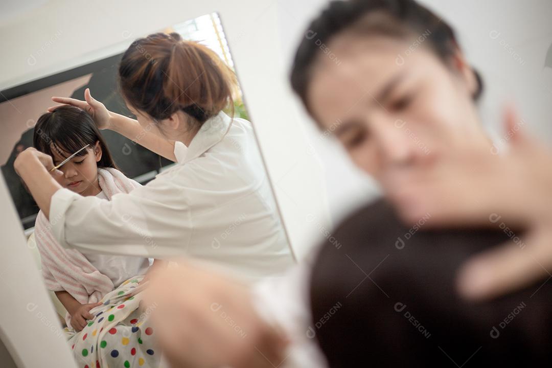 Mãe asiática cortando cabelo para sua filha na sala de estar em casa