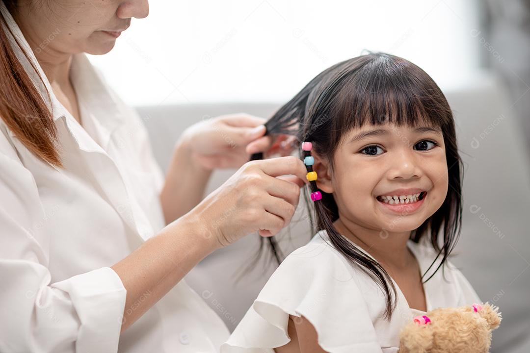 Jovem mãe asiática amarrando o cabelo da filha