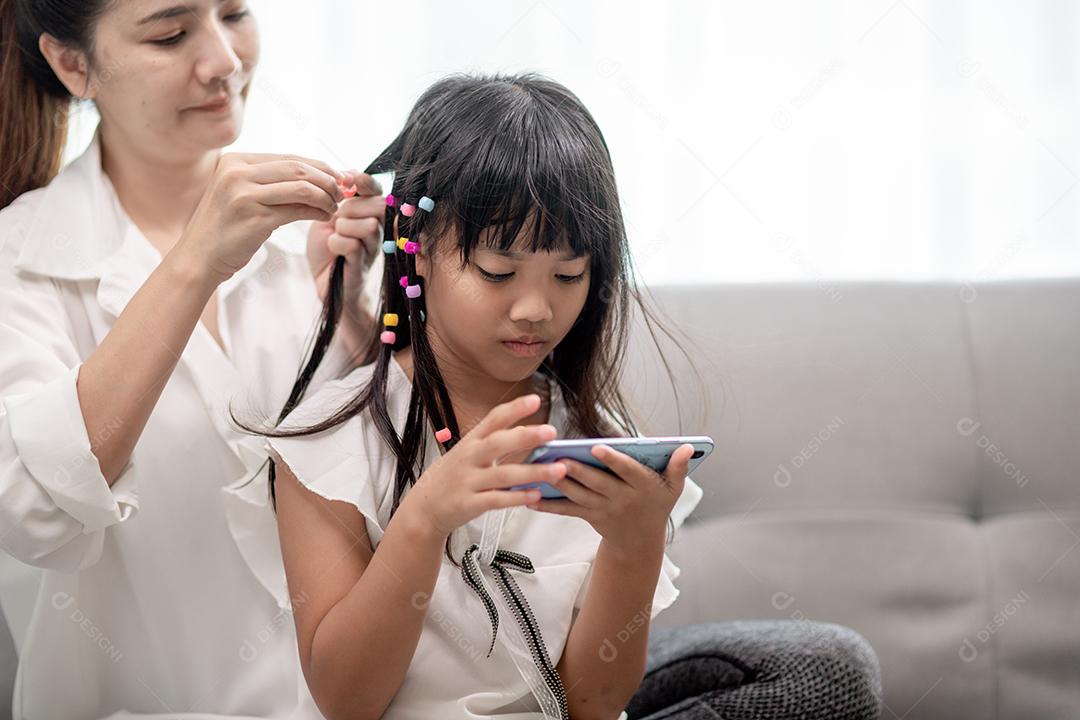 Jovem mãe asiática amarrando o cabelo da filha