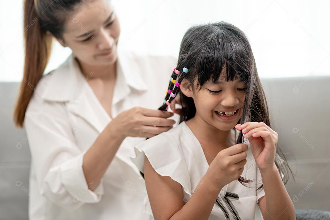 Jovem mãe asiática amarrando o cabelo da filha