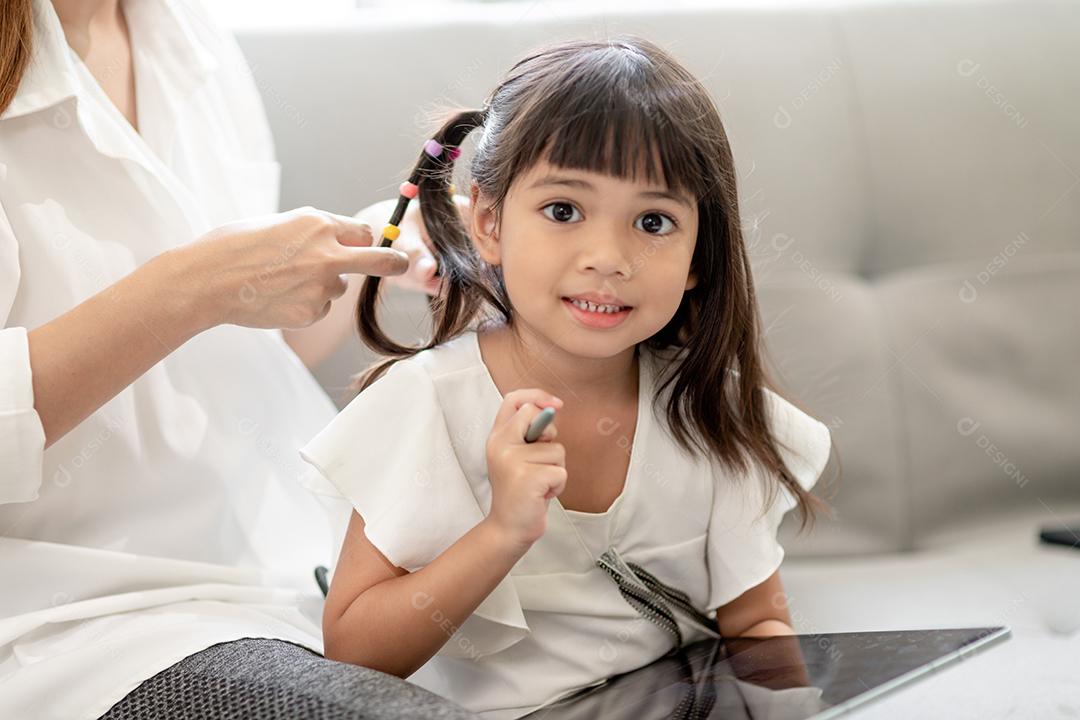 Jovem mãe asiática amarrando o cabelo da filha