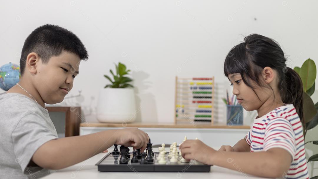 Menino e menina estão jogando xadrez em casa. Crianças jogando xadrez