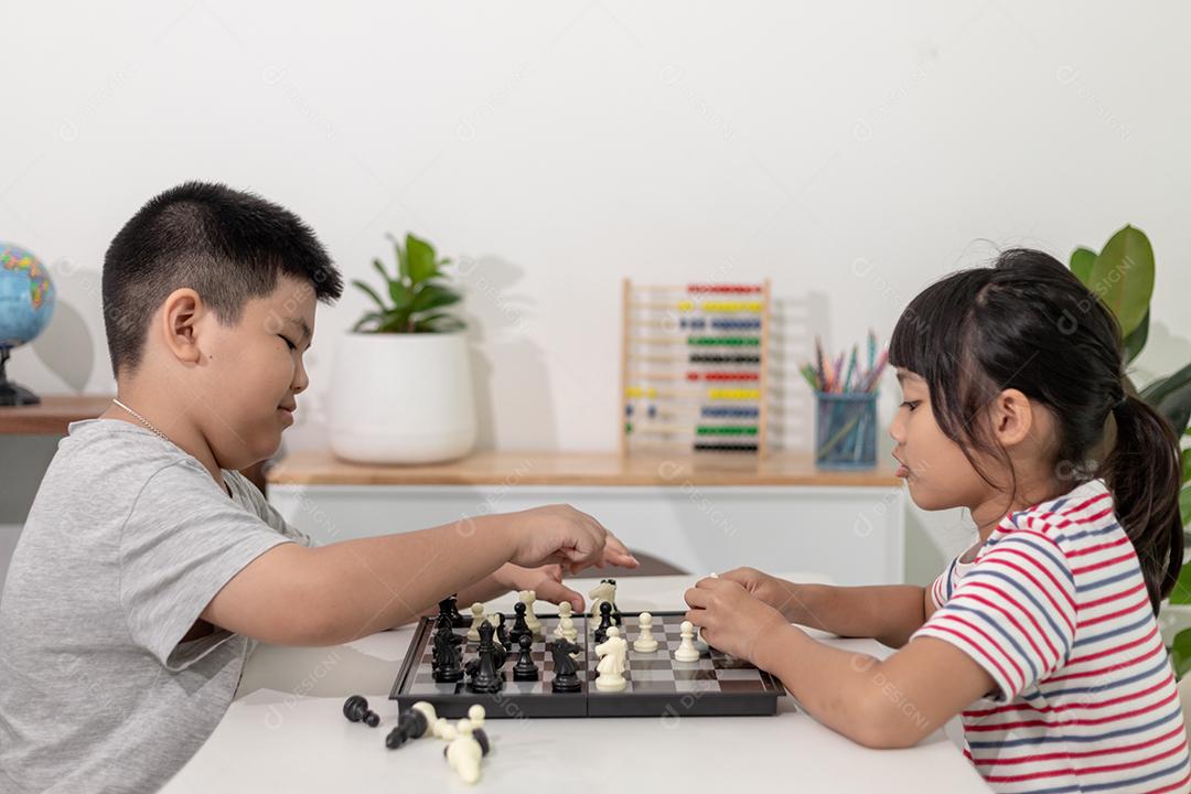 Menino e menina estão jogando xadrez em casa. Crianças jogando xadrez