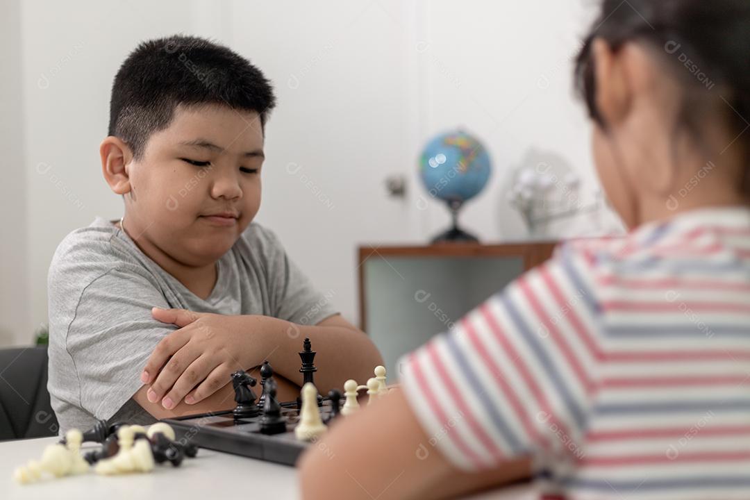 Menino e menina estão jogando xadrez em casa. Crianças jogando xadrez