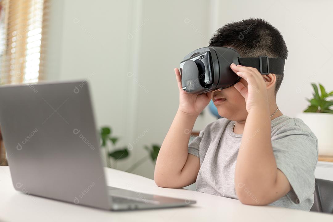 Asian boy with VR glasses studying science at home, curious student wears a virtual reality headset to study science at home online study futuristic lifestyle learning