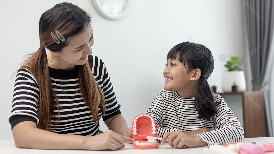 mãe ensinando filha criança escovando os dentes em casa