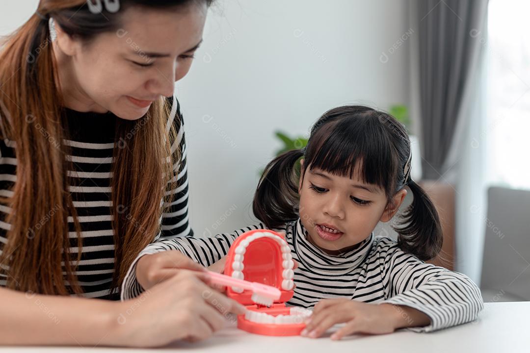 mãe ensinando filha criança escovando os dentes em casa