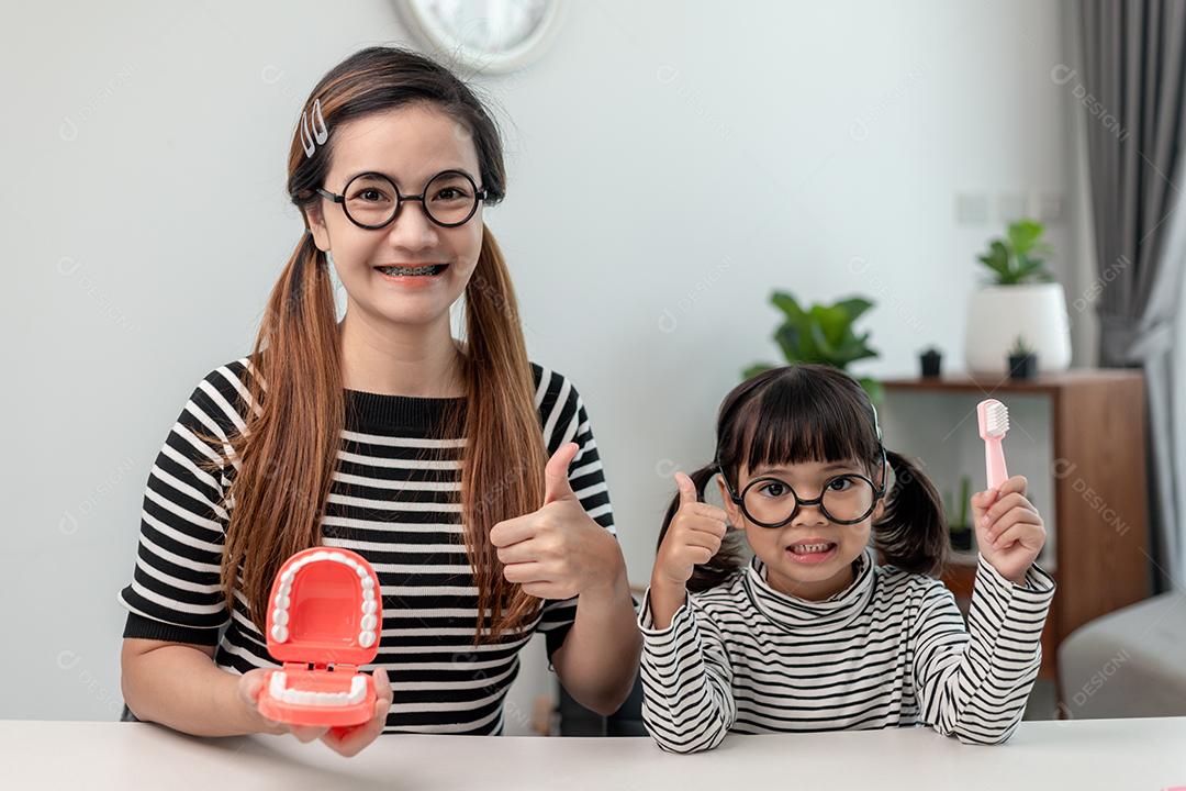 mãe ensinando filha criança escovando os dentes em casa