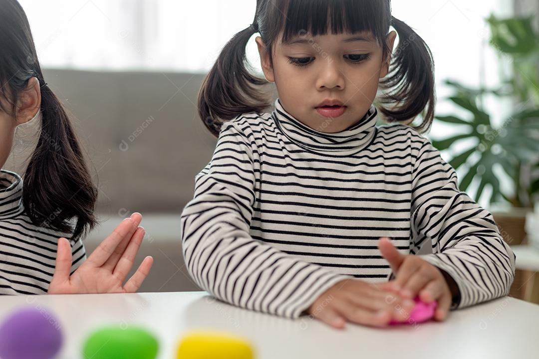A garotinha está aprendendo a usar massinha colorida em uma sala bem iluminada