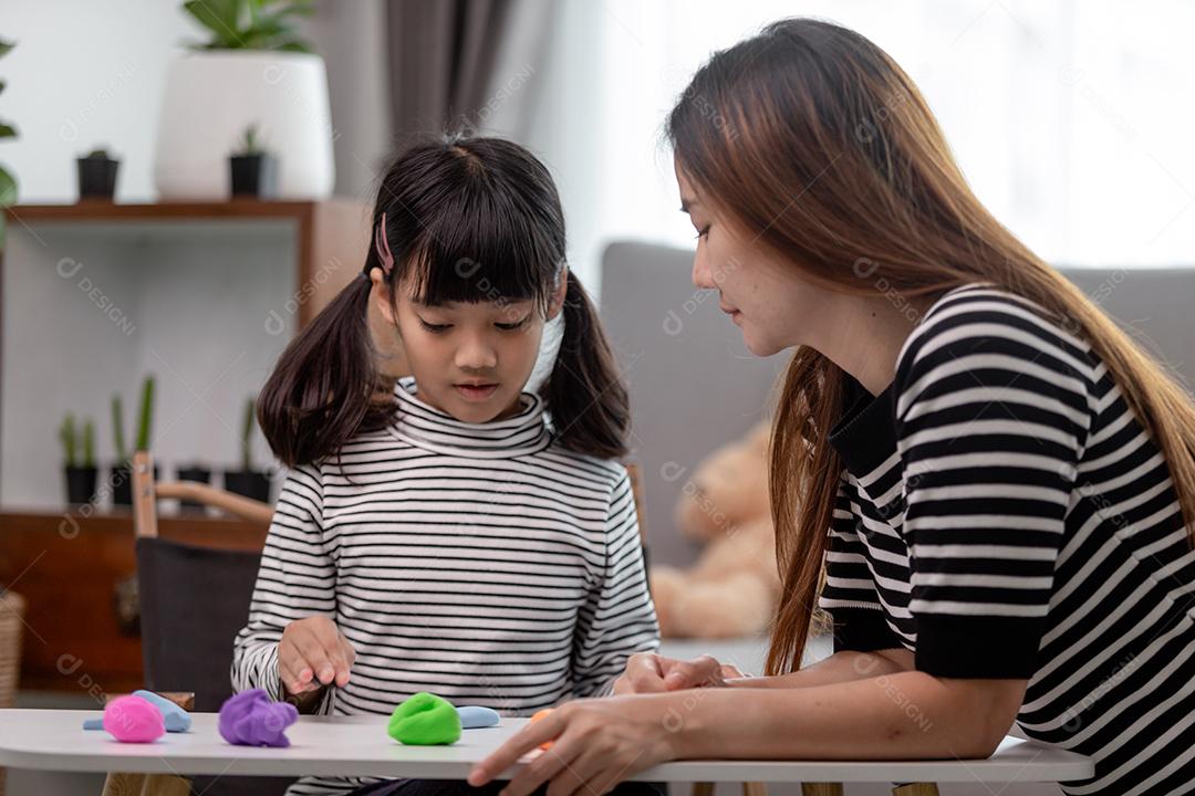 Mãe e filha asiáticas jogam massa de modelar juntas na cozinha com luz do dia e parecem felizes. Conceito de desfrutar com tempo em família