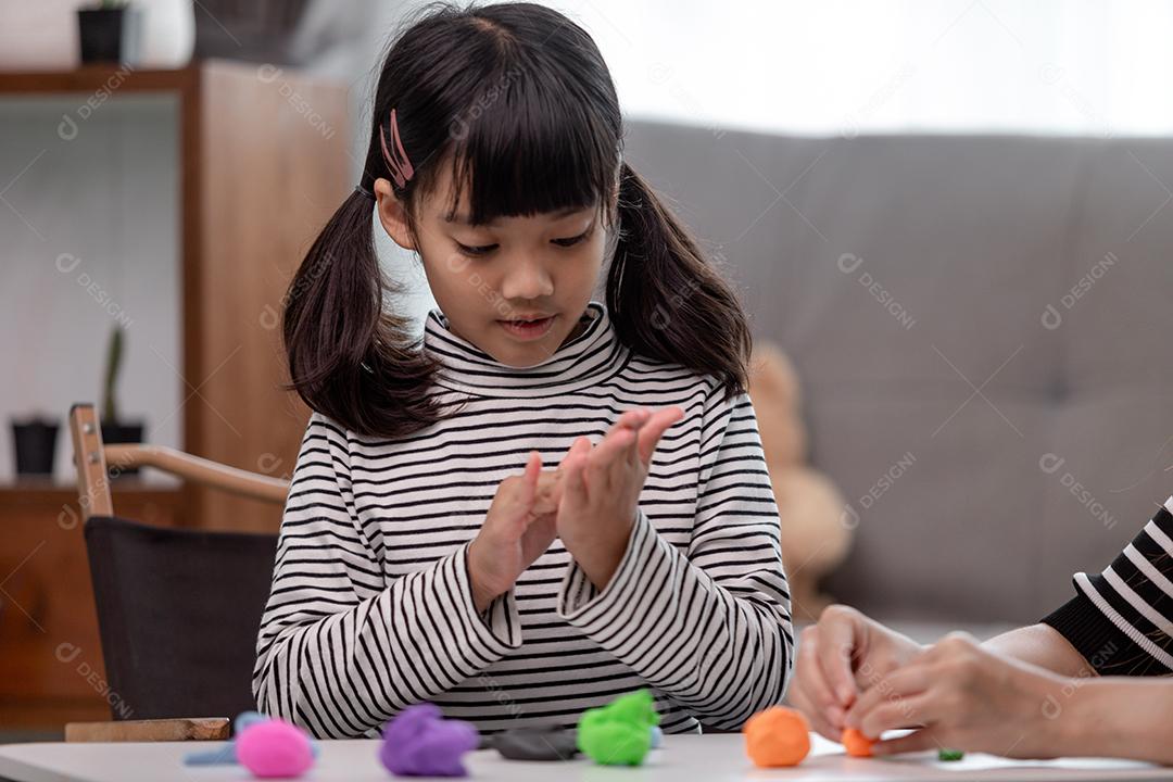 Mãe e filha asiáticas jogam massa de modelar juntas na cozinha com luz do dia e parecem felizes. Conceito de desfrutar com tempo em família