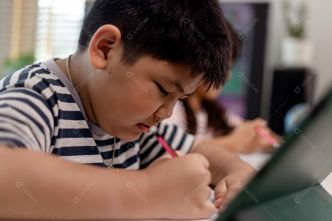 Meninos e meninas asiáticos gostam de aprender online fazendo anotações e usando tablets em casa.