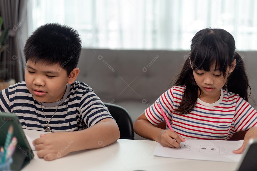 Meninos e meninas asiáticos gostam de aprender online fazendo anotações e usando tablets em casa.