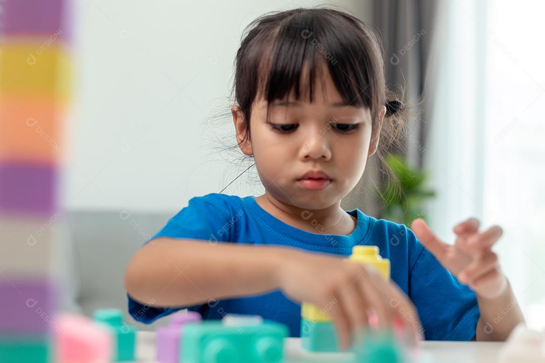 Adorável menina jogando blocos de brinquedo em uma sala iluminada