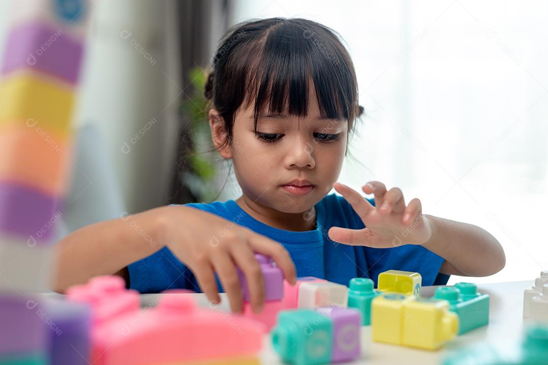 Adorável menina jogando blocos de brinquedo em uma sala iluminada